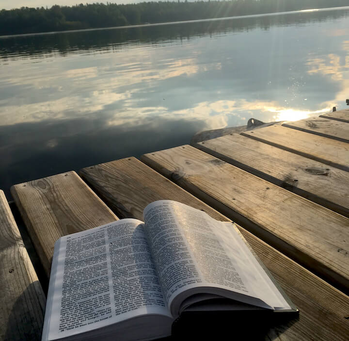 bible laying on a dock with the lake and trees in the background